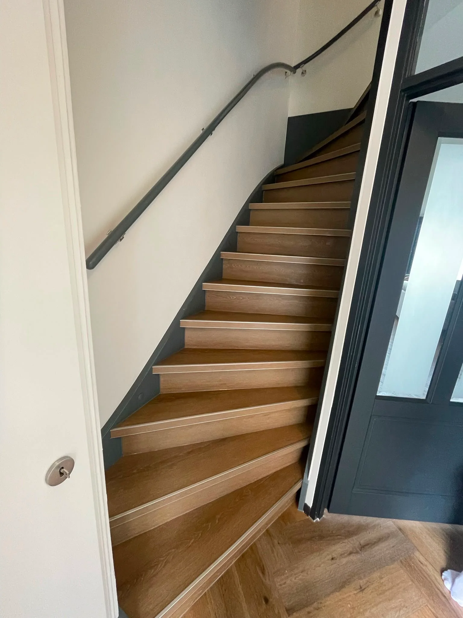 PVC trap in eikenlook langs een donkere wand, met zwarte leuning